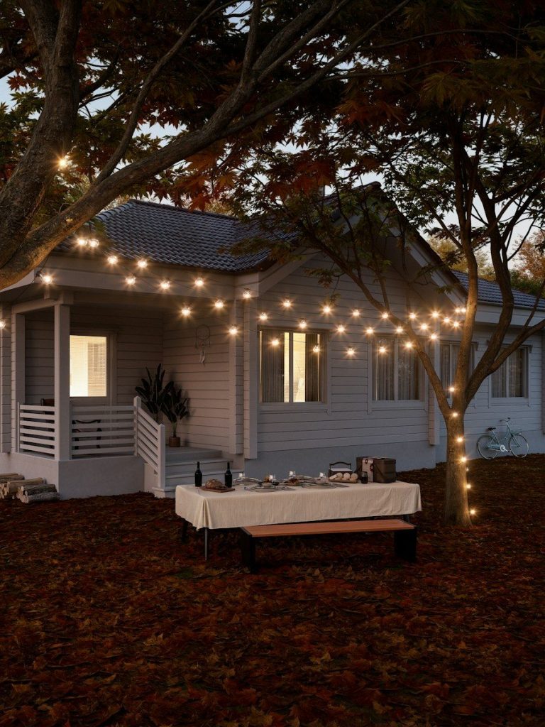 Mesa preparada para una cena en el jardín de casa con guirnaldas de luces